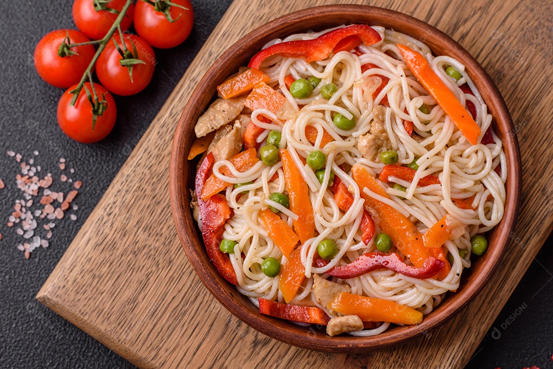 Delicioso macarrão de arroz ou udon com frango, cenoura, pimenta, sal, especiarias e ervas sobre fundo escuro de concreto