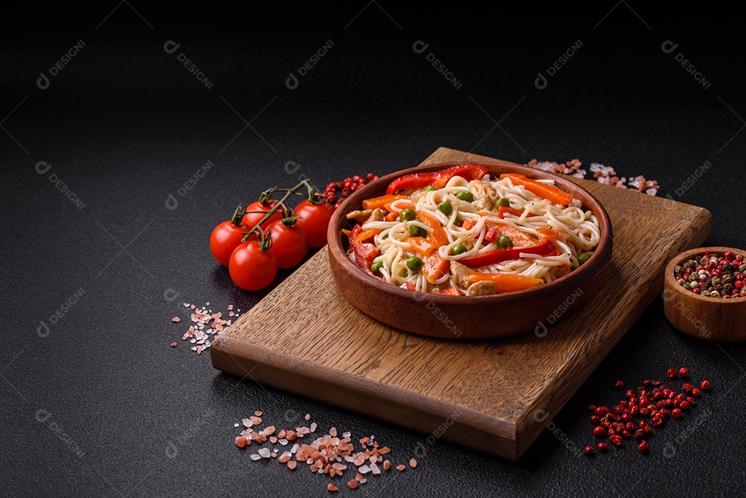 Delicioso macarrão de arroz ou udon com frango, cenoura, pimenta, sal, especiarias e ervas sobre fundo escuro de concreto