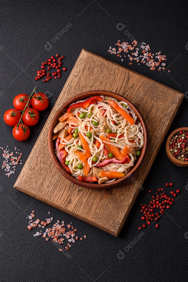 Delicioso macarrão de arroz ou udon com frango, cenoura, pimenta, sal, especiarias e ervas sobre fundo escuro de concreto