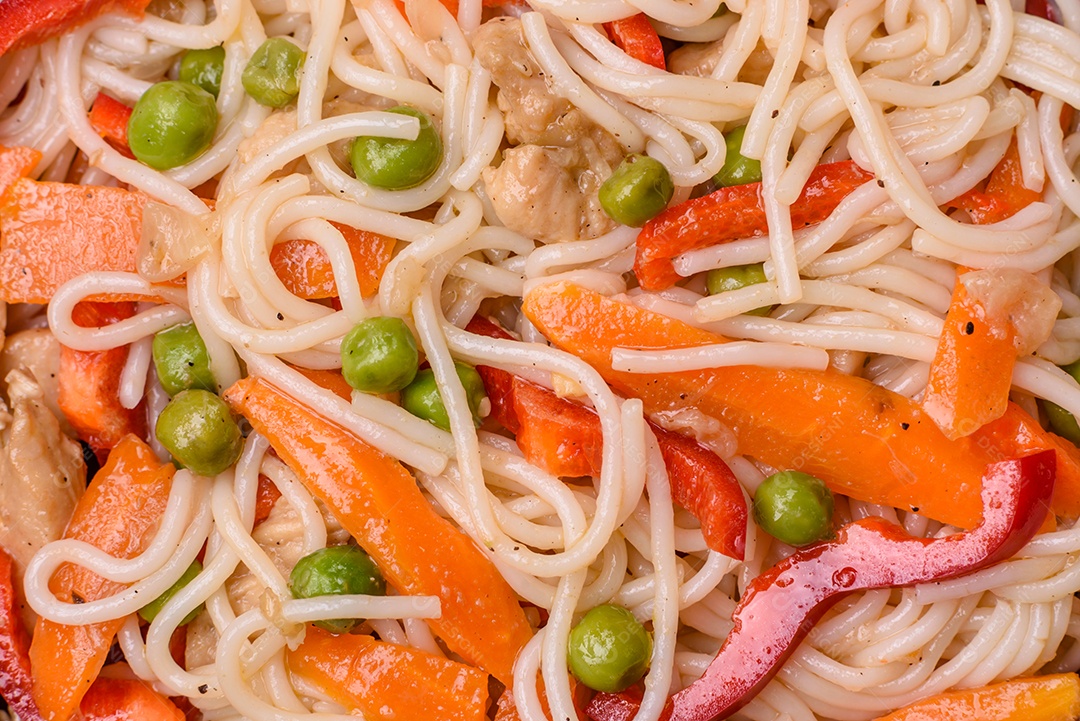 Delicioso macarrão de arroz ou udon com frango, cenoura, pimenta, sal, especiarias e ervas sobre fundo escuro de concreto