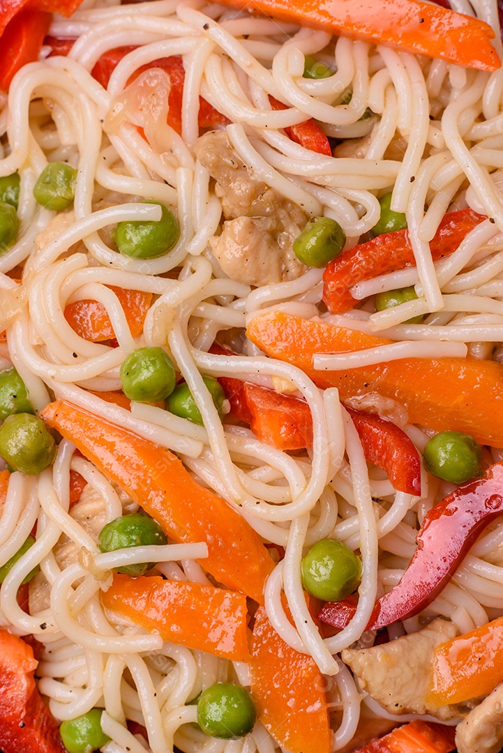 Delicioso macarrão de arroz ou udon com frango, cenoura, pimenta, sal, especiarias e ervas sobre fundo escuro de concreto