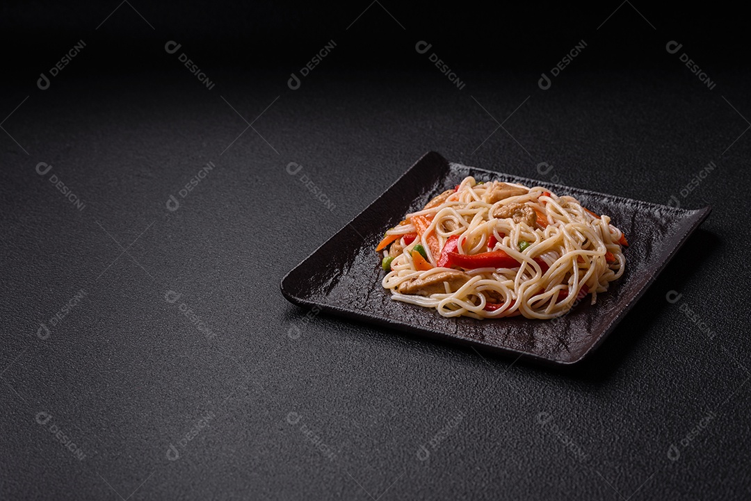 Delicioso macarrão de arroz ou udon com frango, cenoura, pimenta, sal, especiarias e ervas sobre fundo escuro de concreto