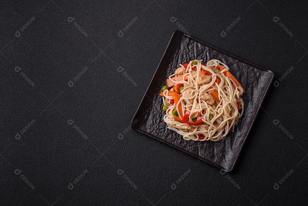 Delicioso macarrão de arroz ou udon com frango, cenoura, pimenta, sal, especiarias e ervas sobre fundo escuro de concreto