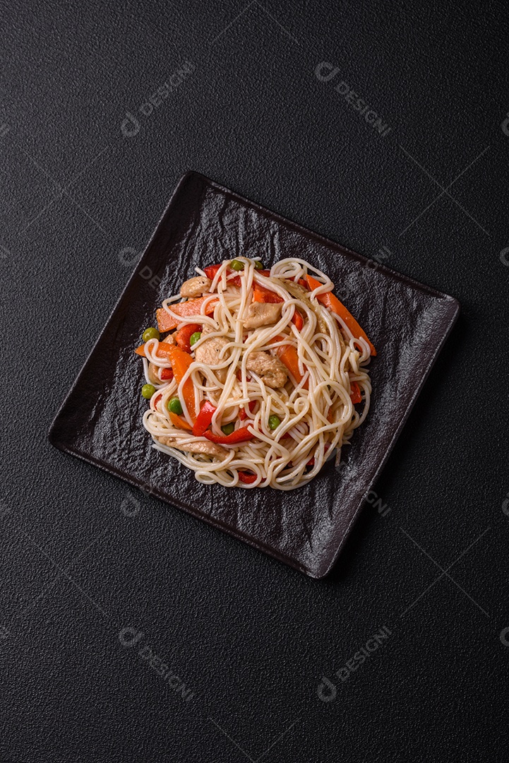 Delicioso macarrão de arroz ou udon com frango, cenoura, pimenta, sal, especiarias e ervas sobre fundo escuro de concreto