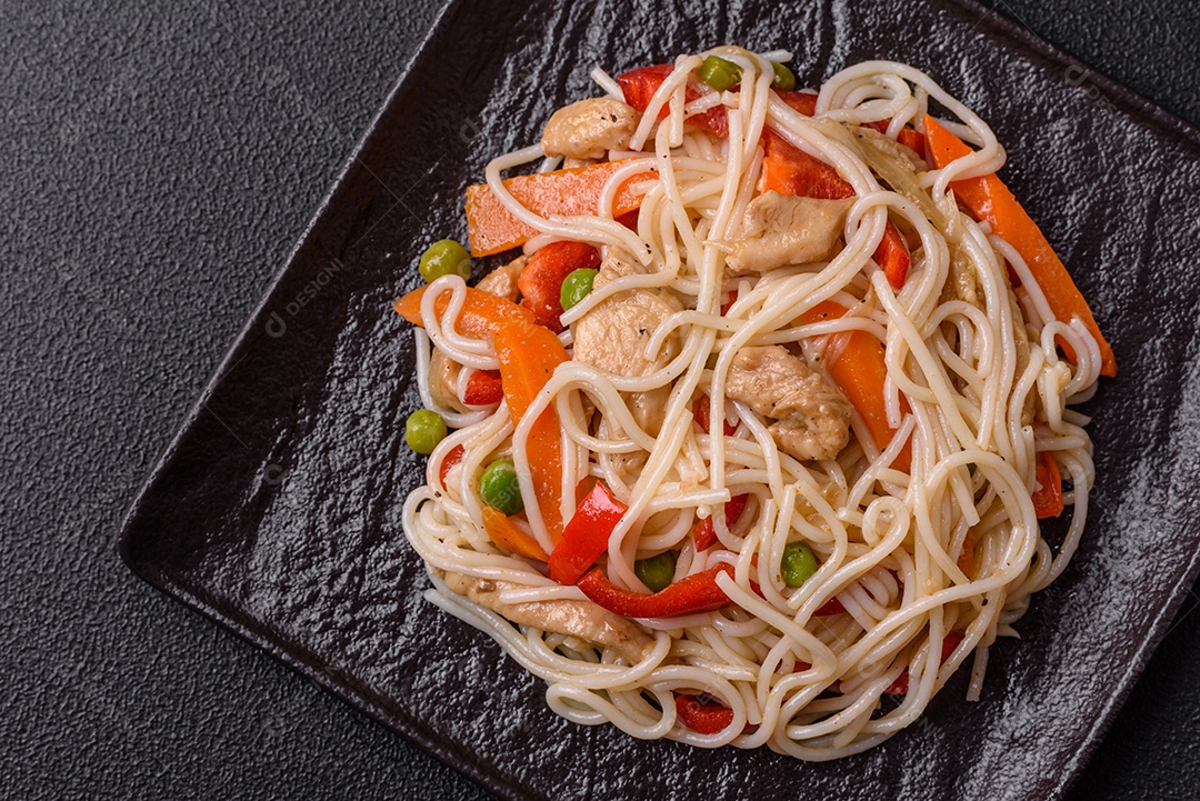 Delicioso macarrão de arroz ou udon com frango, cenoura, pimenta, sal, especiarias e ervas sobre fundo escuro de concreto