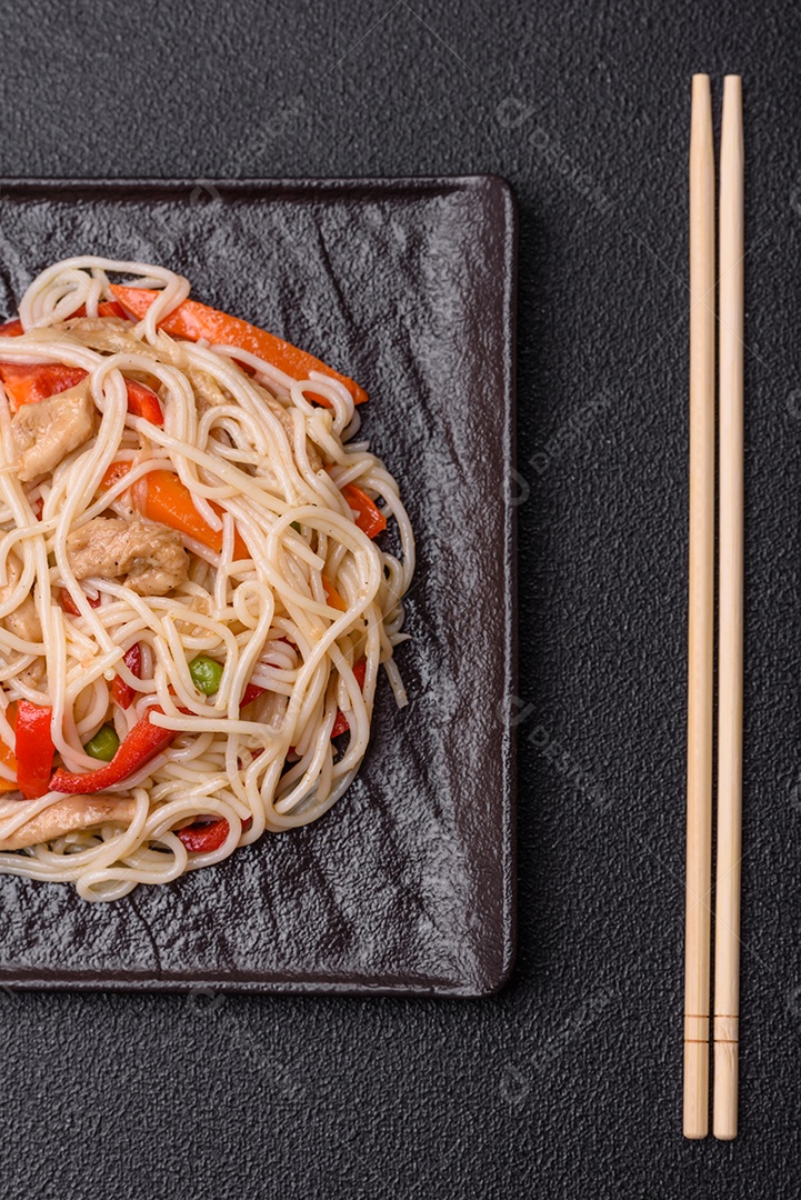 Delicioso macarrão de arroz ou udon com frango, cenoura, pimenta, sal, especiarias e ervas sobre fundo escuro de concreto