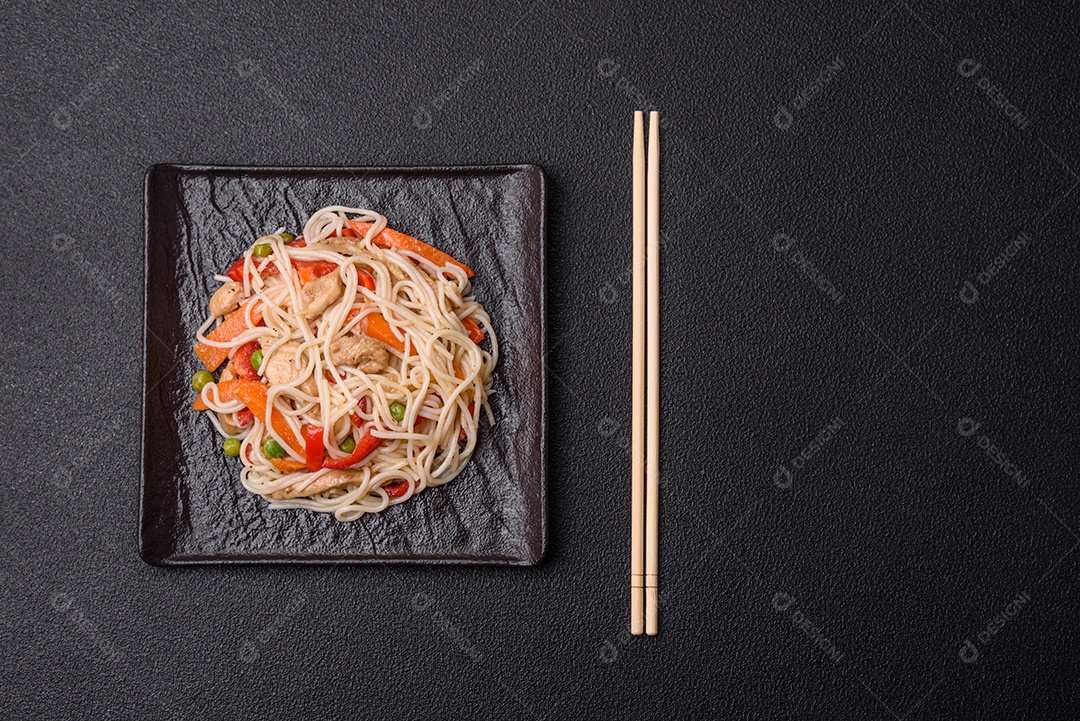 Delicioso macarrão de arroz ou udon com frango, cenoura, pimenta, sal, especiarias e ervas sobre fundo escuro de concreto