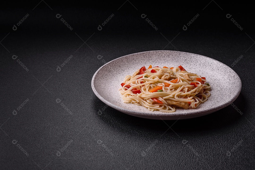 Delicioso macarrão de arroz ou udon com frango, cenoura, pimenta, sal, especiarias e ervas sobre fundo escuro de