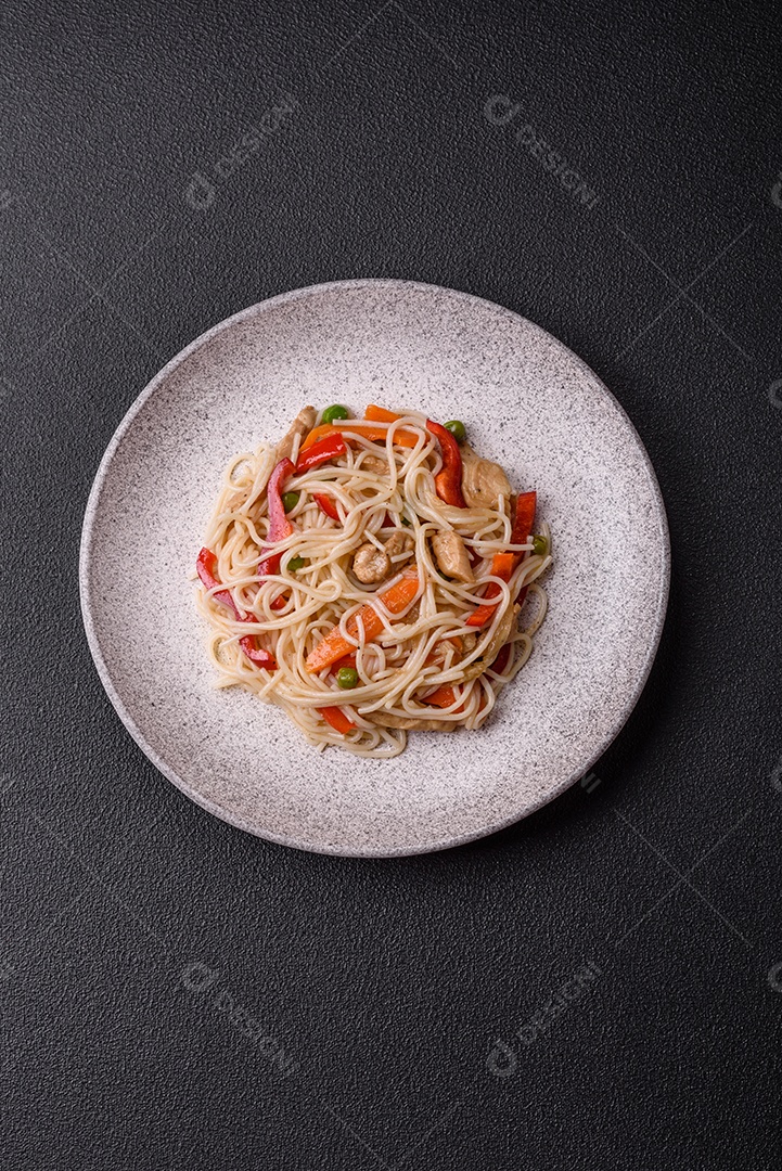 Delicioso macarrão de arroz ou udon com frango, cenoura, pimenta, sal, especiarias e ervas sobre fundo escuro de concreto