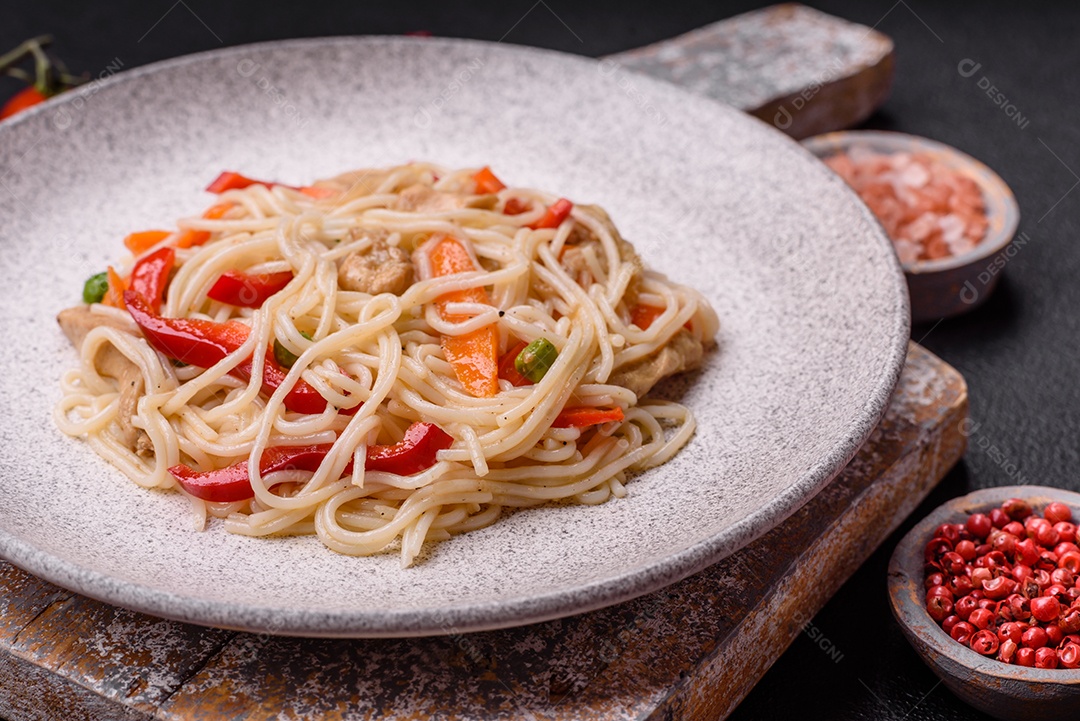 Delicioso macarrão de arroz ou udon com frango, cenoura, pimenta, sal, especiarias e ervas sobre fundo escuro de concreto