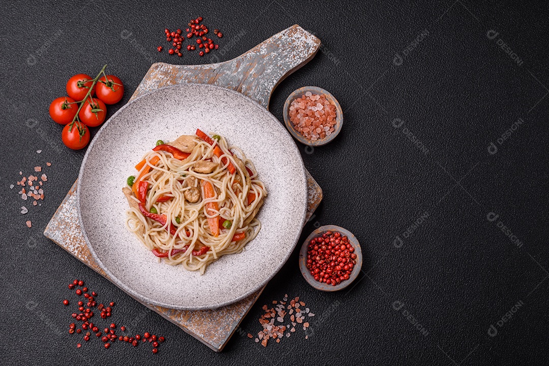 Delicioso macarrão de arroz ou udon com frango, cenoura, pimenta, sal, especiarias e ervas sobre fundo escuro de concreto