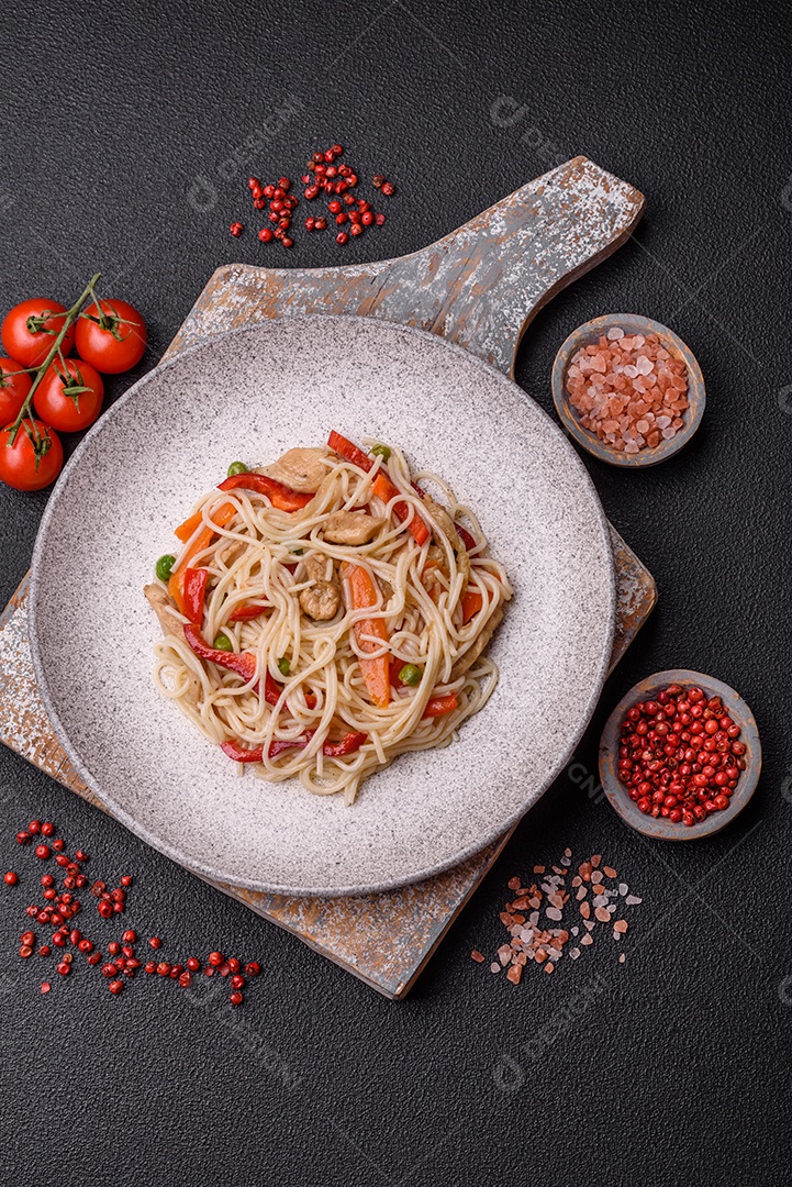 Delicioso macarrão de arroz ou udon com frango, cenoura, pimenta, sal, especiarias e ervas sobre fundo escuro de concreto