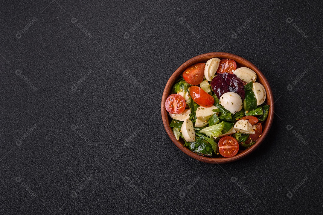 Deliciosa salada caprese fresca com mussarela, tomate, verduras com sal, especiarias e ervas sobre fundo escuro de concreto