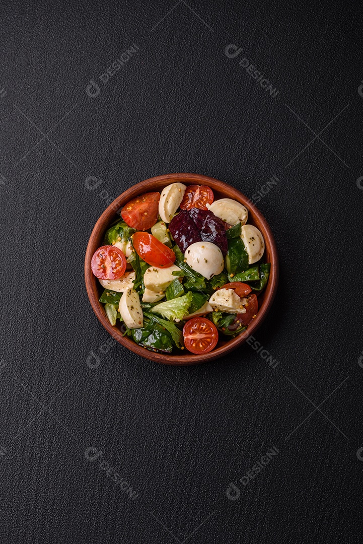 Deliciosa salada caprese fresca com mussarela, tomate, verduras com sal, especiarias e ervas sobre fundo escuro de concreto