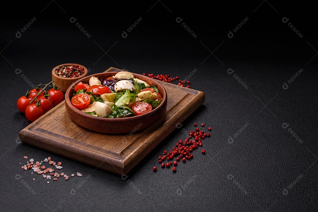 Deliciosa salada caprese fresca com mussarela, tomate, verduras com sal, especiarias e ervas sobre fundo escuro de concreto