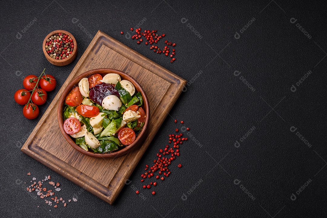 Deliciosa salada caprese fresca com mussarela, tomate, verduras com sal, especiarias e ervas sobre fundo escuro de concreto