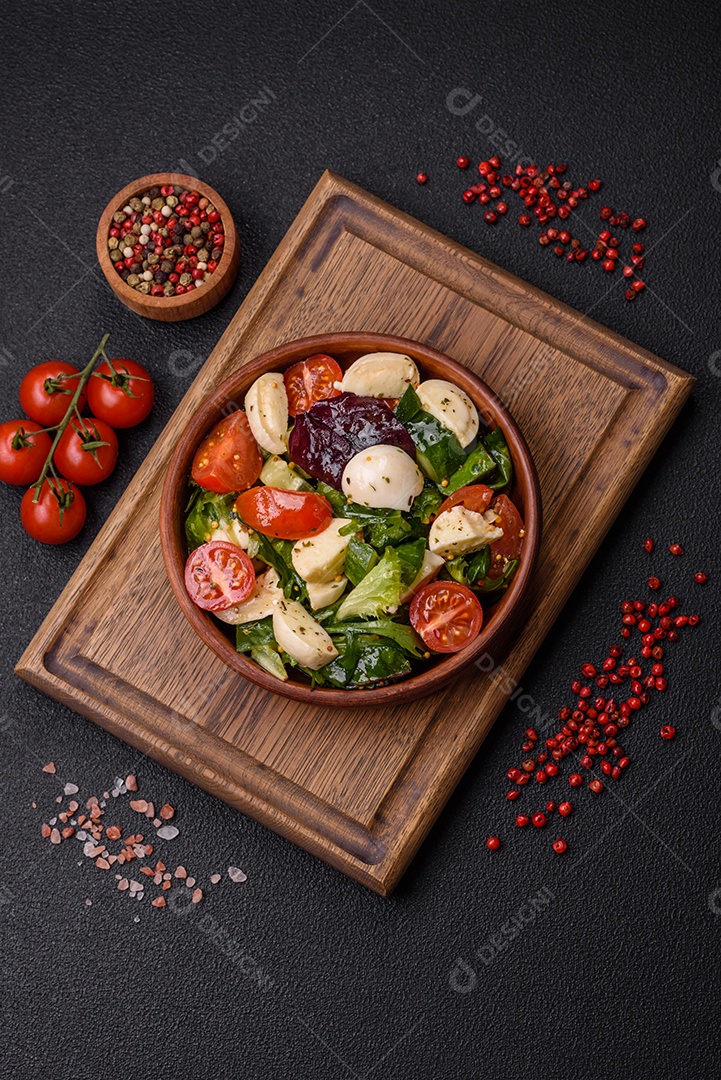 Deliciosa salada caprese fresca com mussarela, tomate, verduras com sal, especiarias e ervas sobre fundo escuro de concreto