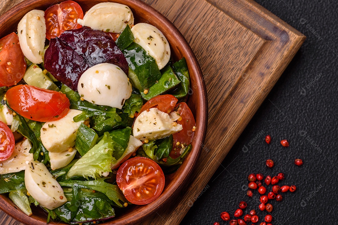 Deliciosa salada caprese fresca com mussarela, tomate, verduras com sal, especiarias e ervas sobre fundo escuro de concreto