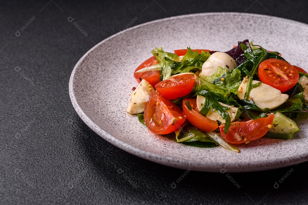 Deliciosa salada caprese fresca com mussarela, tomate, verduras com sal, especiarias e ervas sobre fundo escuro de concreto