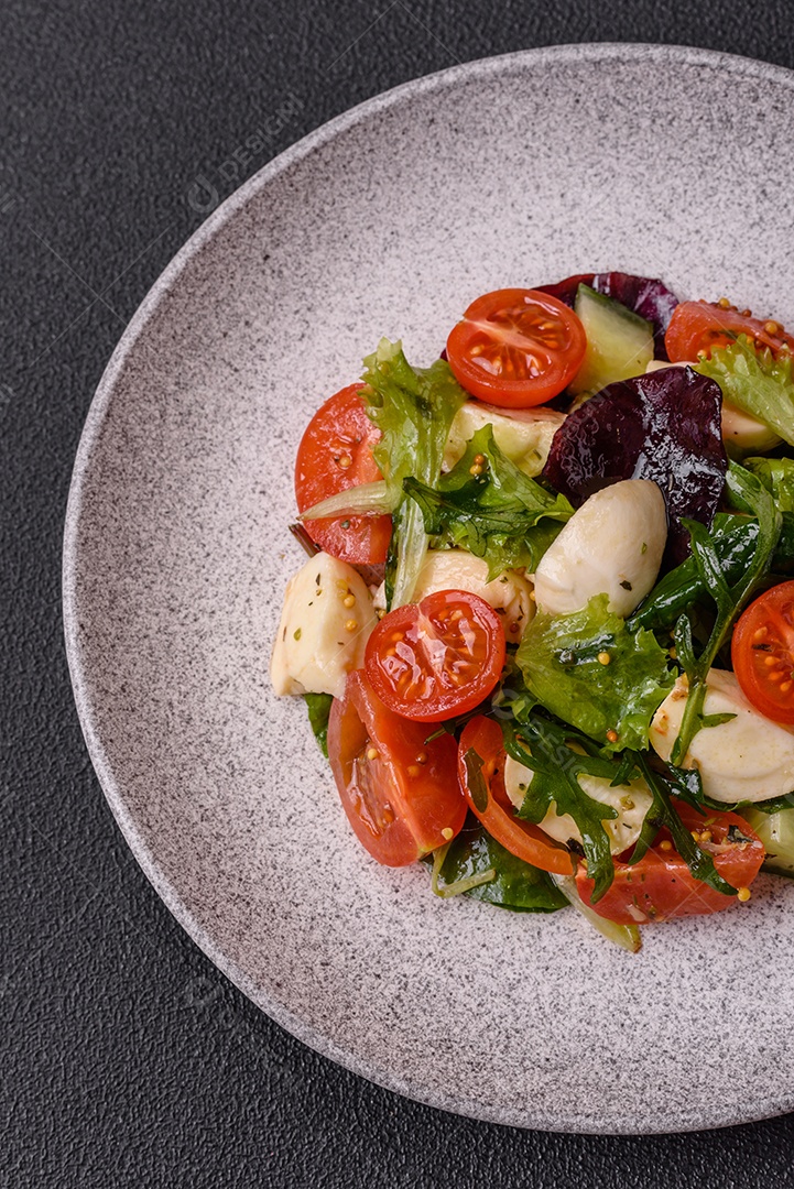 Deliciosa salada caprese fresca com mussarela, tomate, verduras com sal, especiarias e ervas sobre fundo escuro de concreto