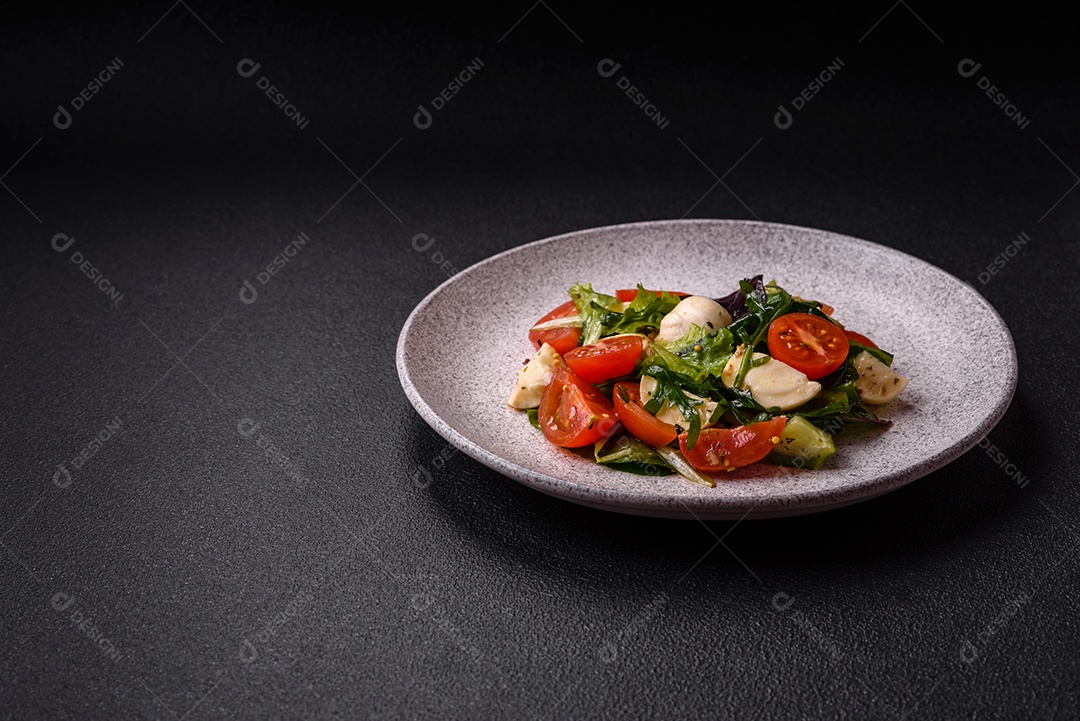 Deliciosa salada caprese fresca com mussarela, tomate, verduras com sal, especiarias e ervas sobre fundo escuro de concreto