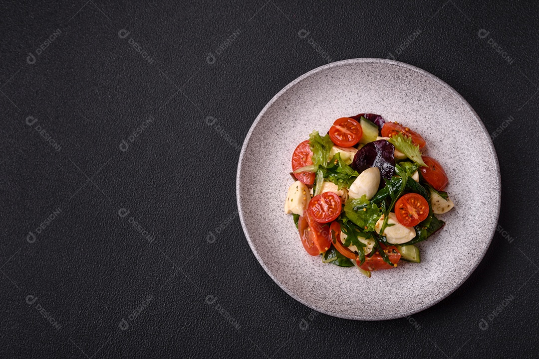 Deliciosa salada caprese fresca com mussarela, tomate, verduras com sal, especiarias e ervas sobre fundo escuro de concreto