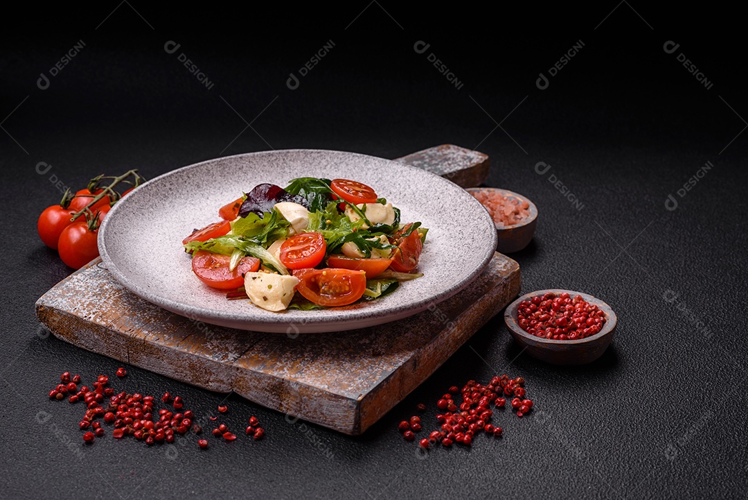 Deliciosa salada caprese fresca com mussarela, tomate, verduras com sal, especiarias e ervas sobre fundo escuro de concreto