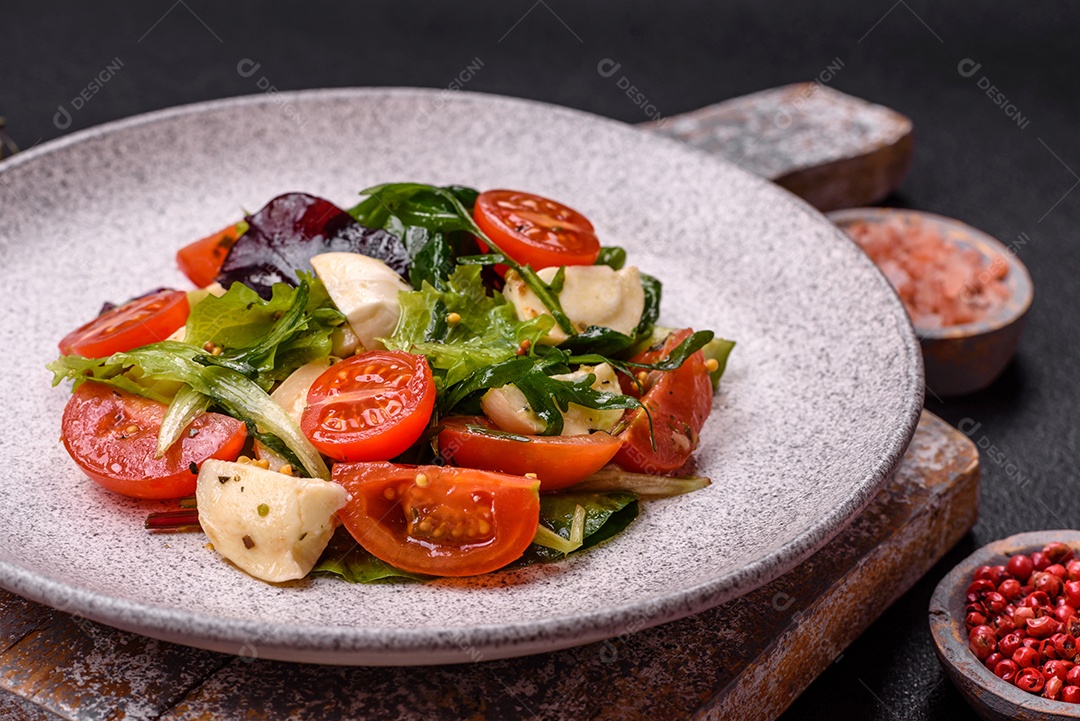Deliciosa salada caprese fresca com mussarela, tomate, verduras com sal, especiarias e ervas sobre fundo escuro de concreto