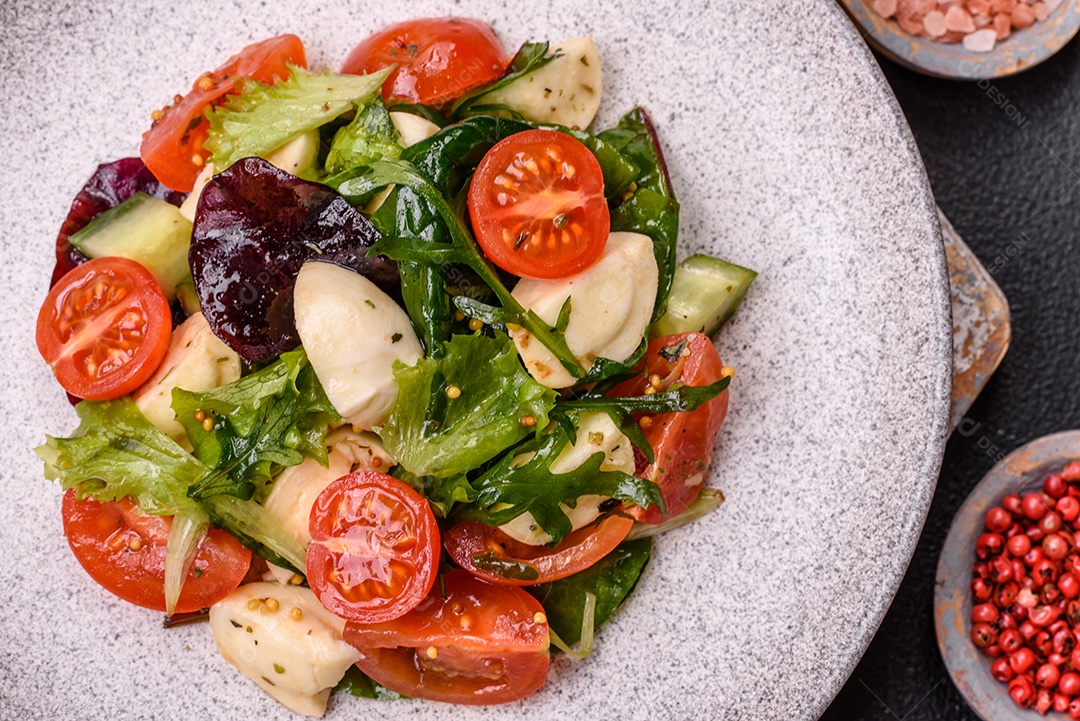 Deliciosa salada caprese fresca com mussarela, tomate, verduras com sal, especiarias e ervas sobre fundo escuro de concreto