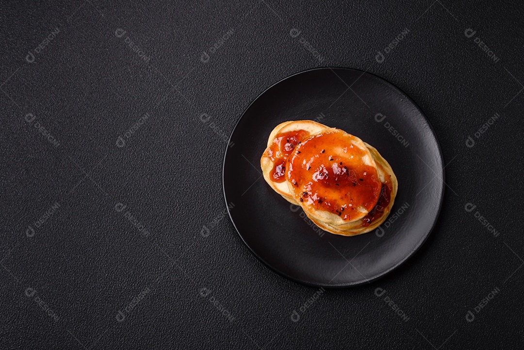 Panquecas recém-assadas com geléia deliciosa em uma placa de cerâmica sobre um fundo escuro de concreto