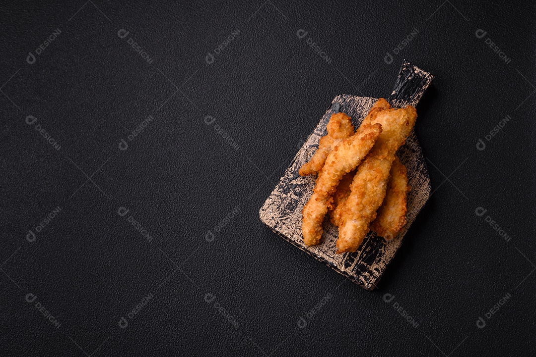 Deliciosas tiras de frango ou peru fresco ou nuggets empanados com sal e especiarias sobre um fundo escuro de concreto