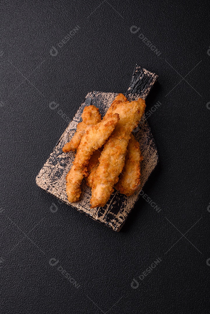Deliciosas tiras de frango ou peru fresco ou nuggets empanados com sal e especiarias sobre um fundo escuro de concreto