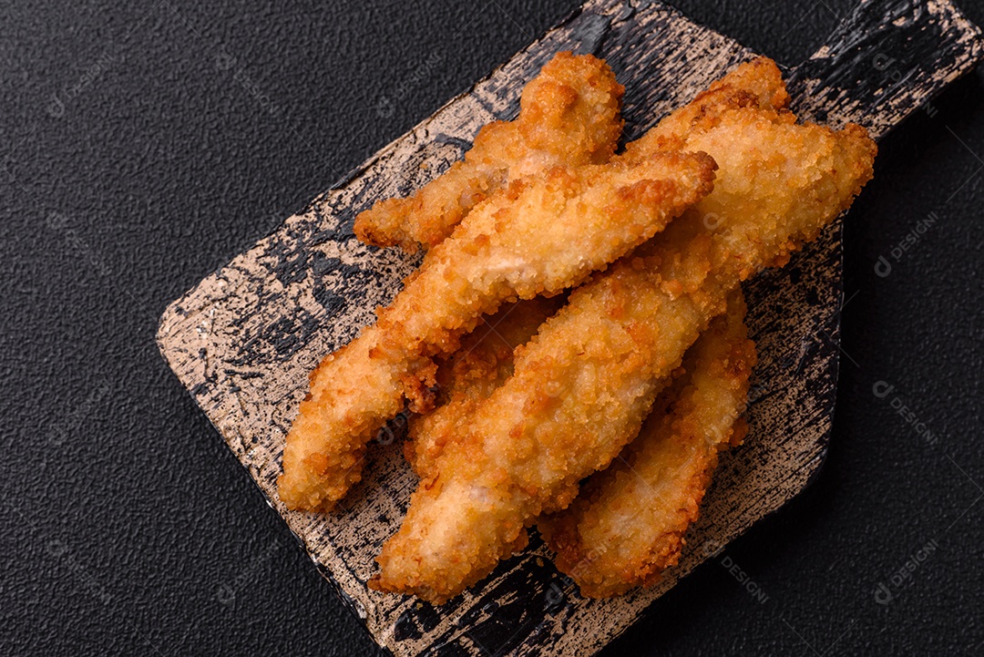 Deliciosas tiras de frango ou peru fresco ou nuggets empanados com sal e especiarias sobre um fundo escuro de concreto