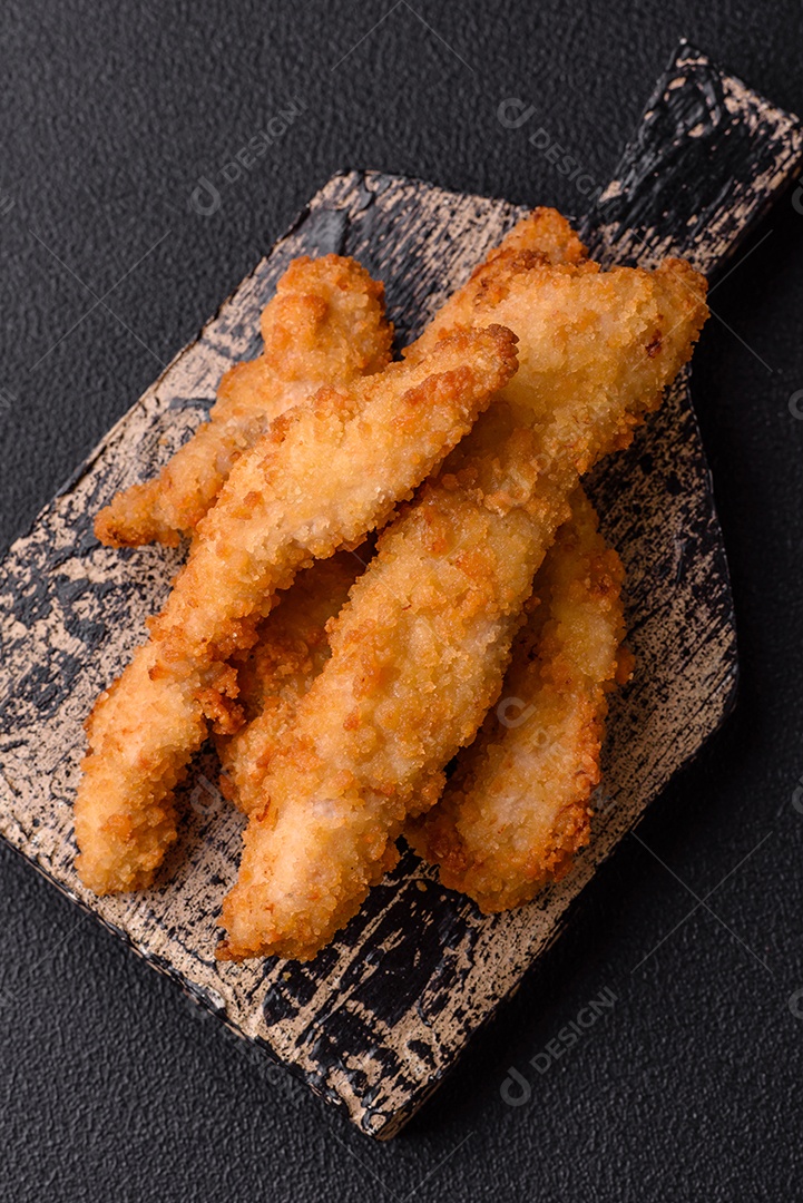 Deliciosas tiras de frango ou peru fresco ou nuggets empanados com sal e especiarias sobre um fundo escuro de concreto