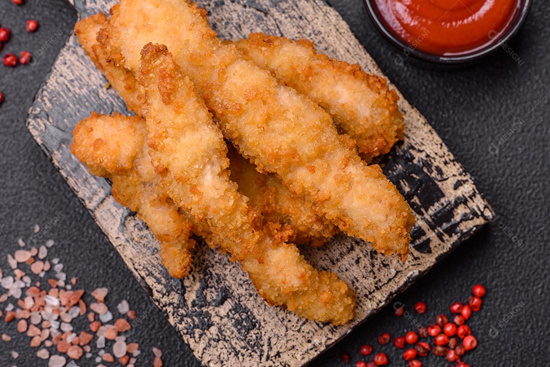 Deliciosas tiras de frango ou peru fresco ou nuggets empanados com sal e especiarias sobre um fundo escuro de concreto