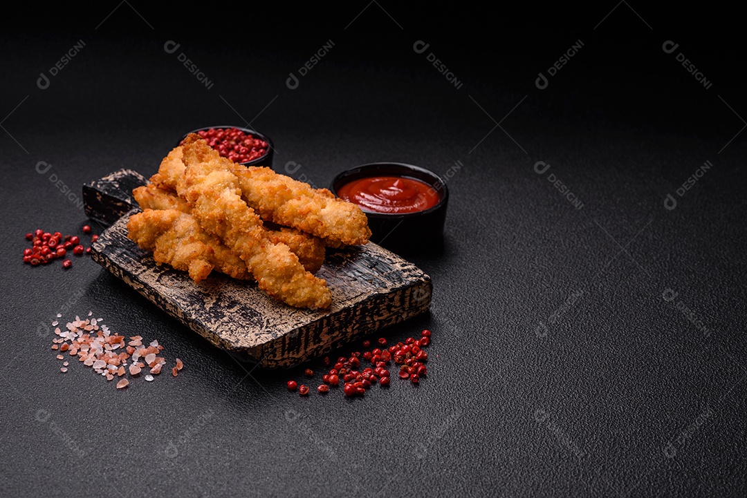 Deliciosas tiras de frango ou peru fresco ou nuggets empanados com sal e especiarias sobre um fundo escuro de concreto