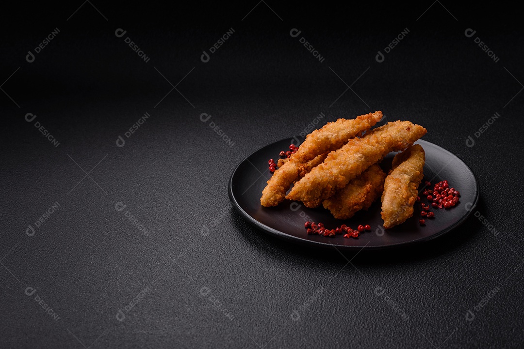 Deliciosas tiras de frango ou peru fresco ou nuggets empanados com sal e especiarias sobre um fundo escuro de concreto