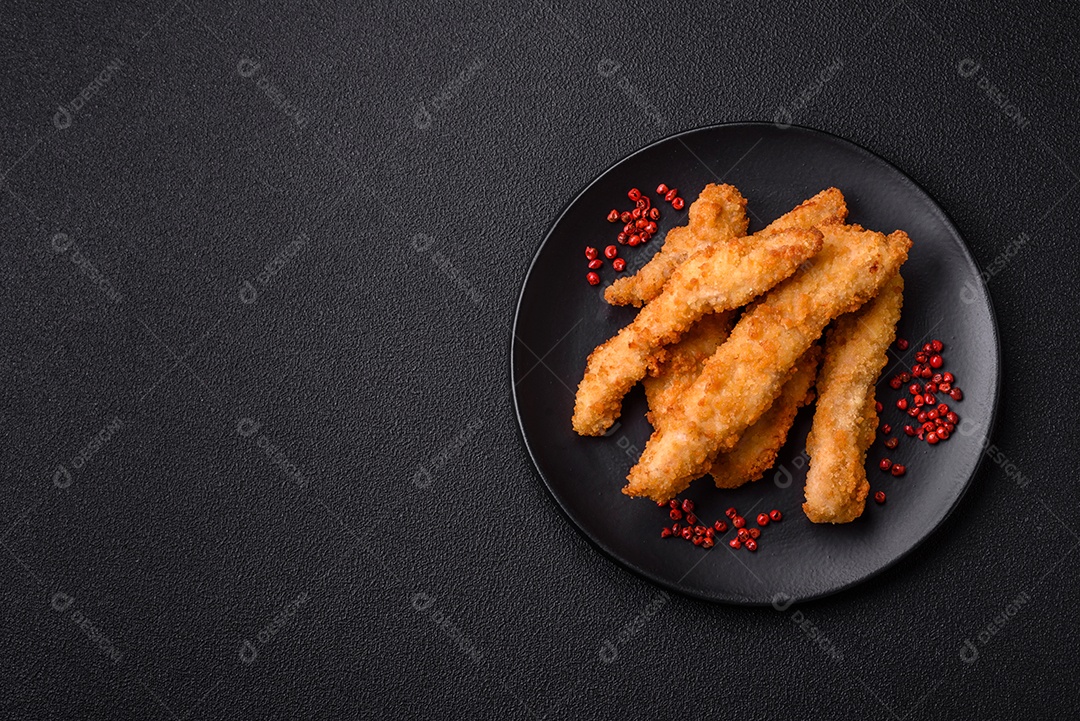 Deliciosas tiras de frango ou peru fresco ou nuggets empanados com sal e especiarias sobre um fundo escuro de concreto