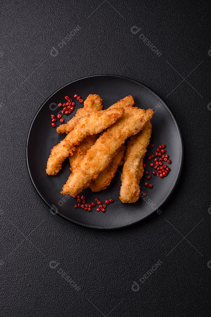 Deliciosas tiras de frango ou peru fresco ou nuggets empanados com sal e especiarias sobre um fundo escuro de concreto