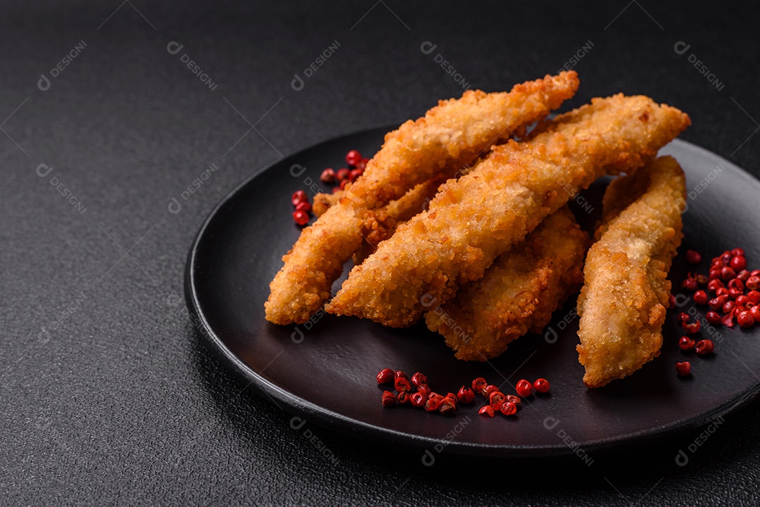 Deliciosas tiras de frango ou peru fresco ou nuggets empanados com sal e especiarias sobre um fundo escuro de concreto
