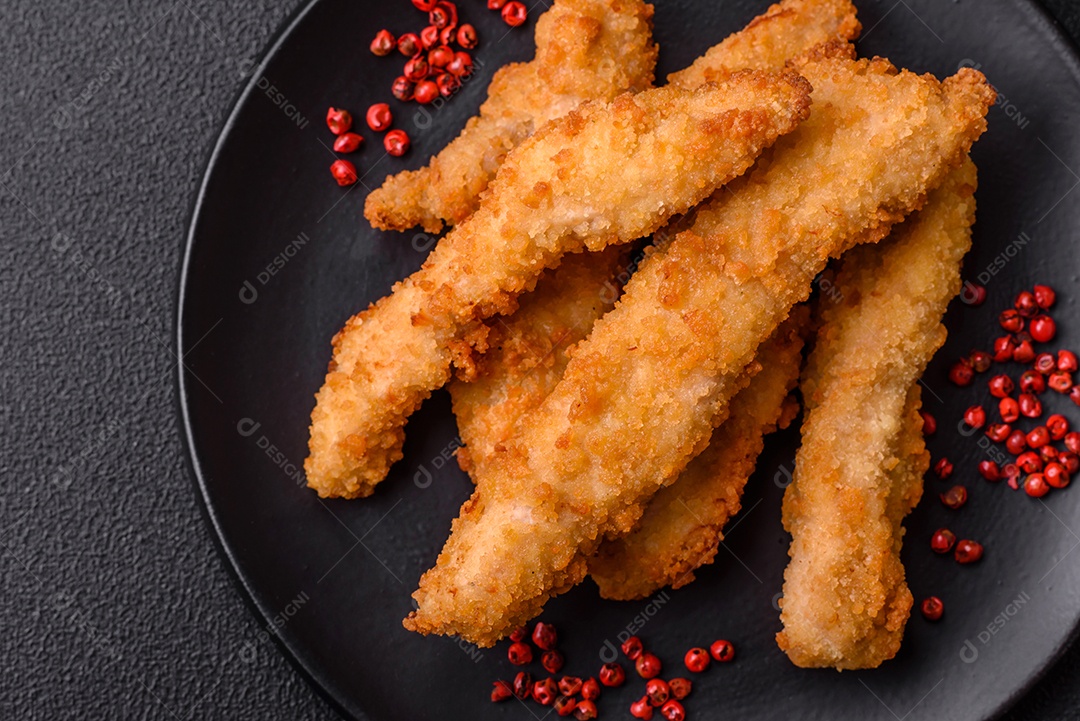 Deliciosas tiras de frango ou peru fresco ou nuggets empanados com sal e especiarias sobre um fundo escuro de concreto