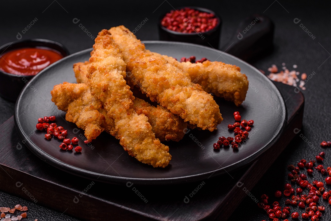 Deliciosas tiras de frango ou peru fresco ou nuggets empanados com sal e especiarias sobre um fundo escuro de concreto