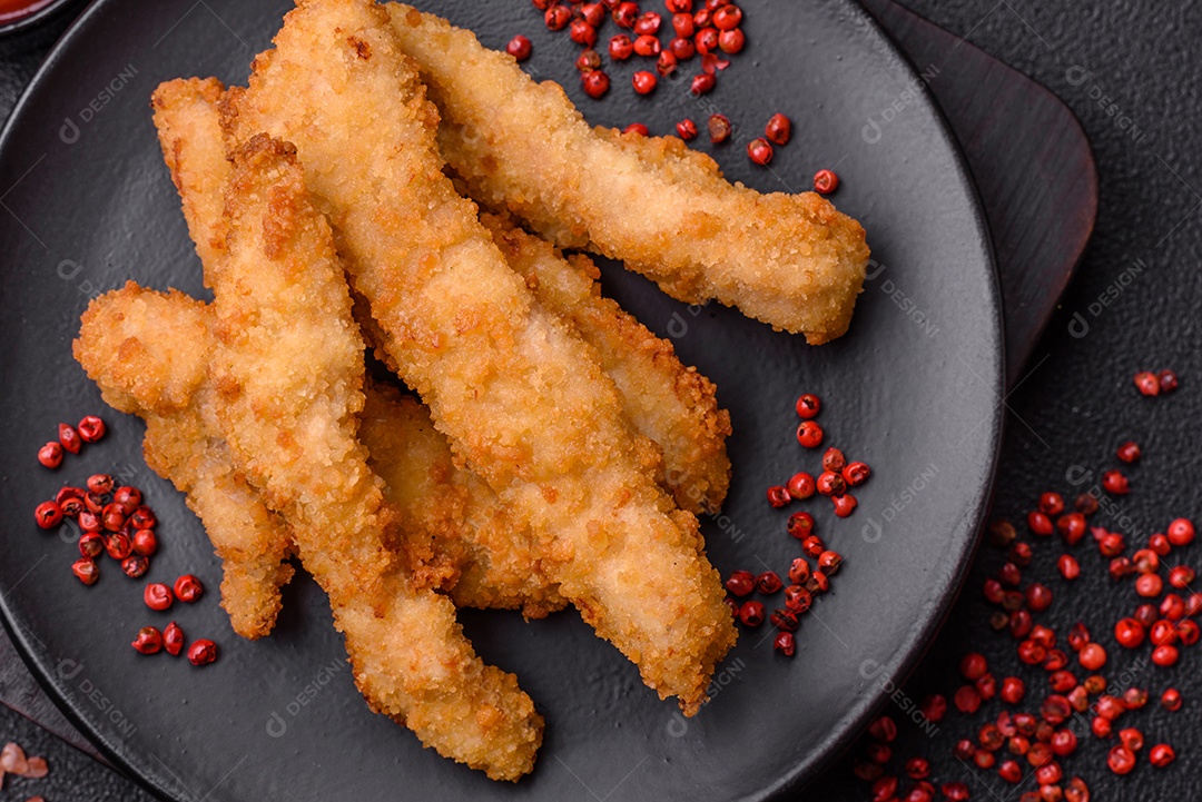 Deliciosas tiras de frango ou peru fresco ou nuggets empanados com sal e especiarias sobre um fundo escuro de concreto