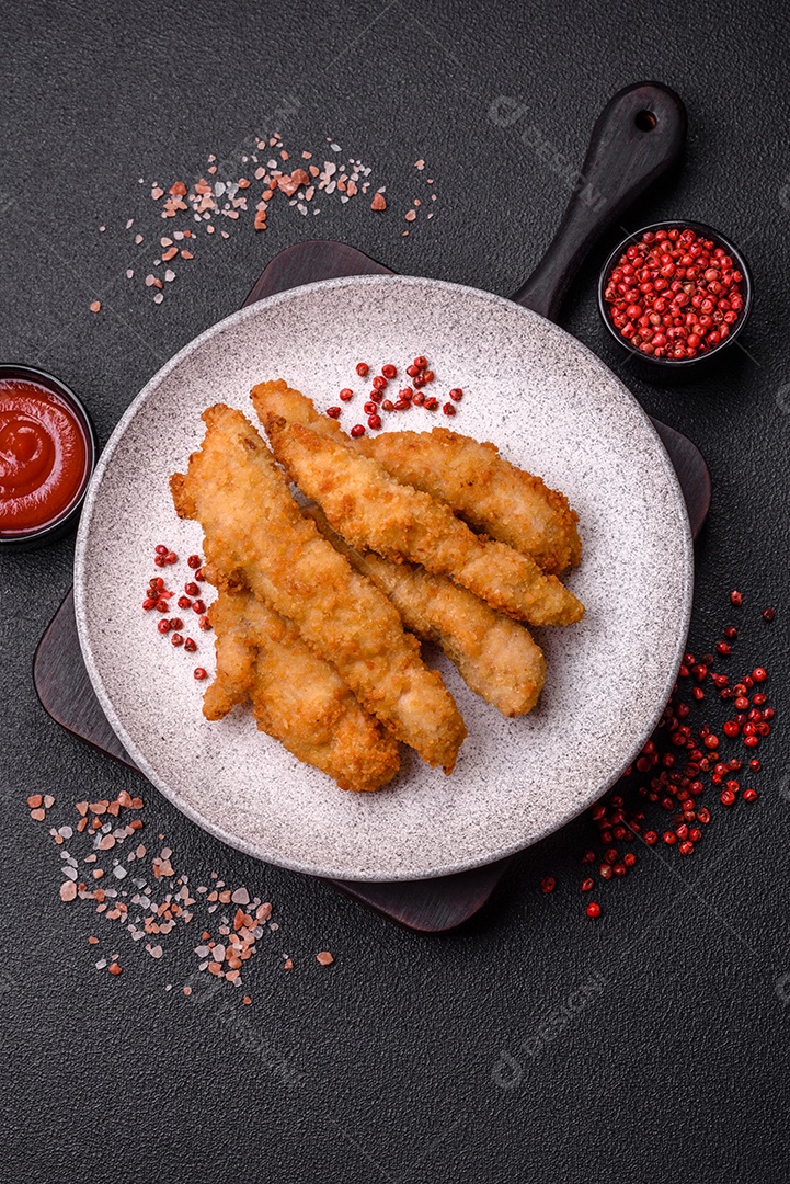 Deliciosas tiras de frango ou peru fresco ou nuggets empanados com sal e especiarias sobre um fundo escuro de concreto