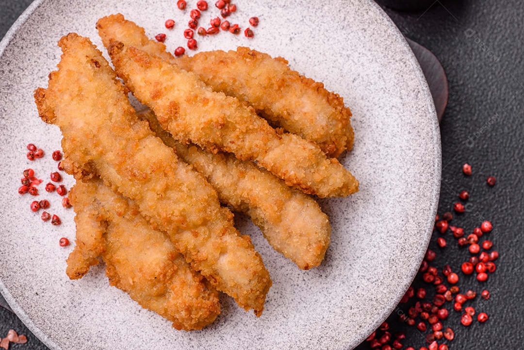 Deliciosas tiras de frango ou peru fresco ou nuggets empanados com sal e especiarias sobre um fundo escuro de concreto