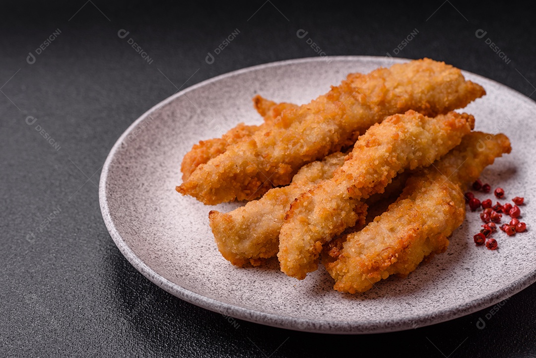 Deliciosas tiras de frango ou peru fresco ou nuggets empanados com sal e especiarias sobre um fundo escuro de concreto