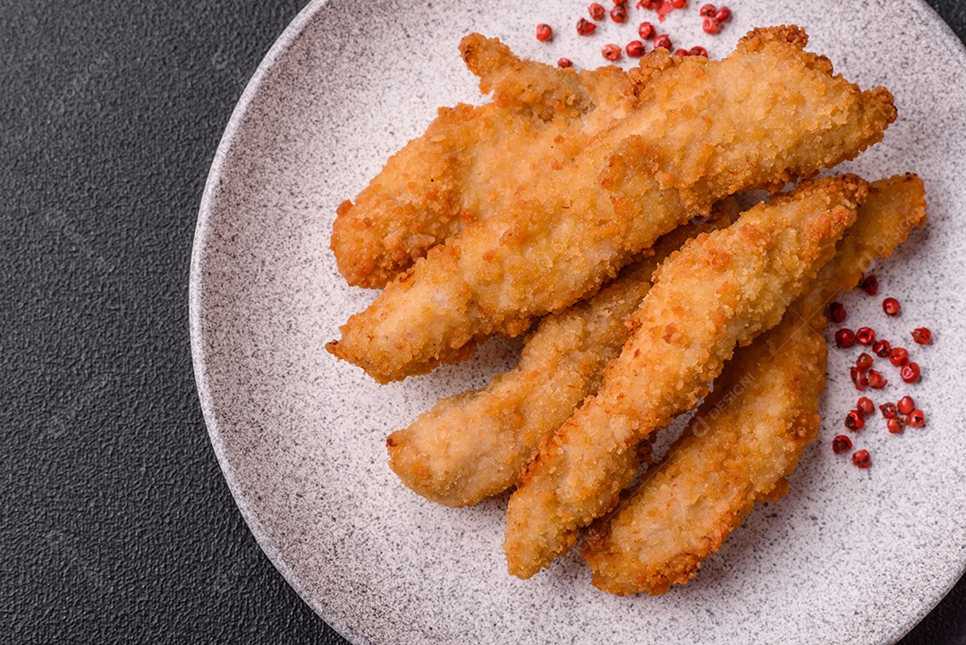 Deliciosas tiras de frango ou peru fresco ou nuggets empanados com sal e especiarias sobre um fundo escuro de concreto