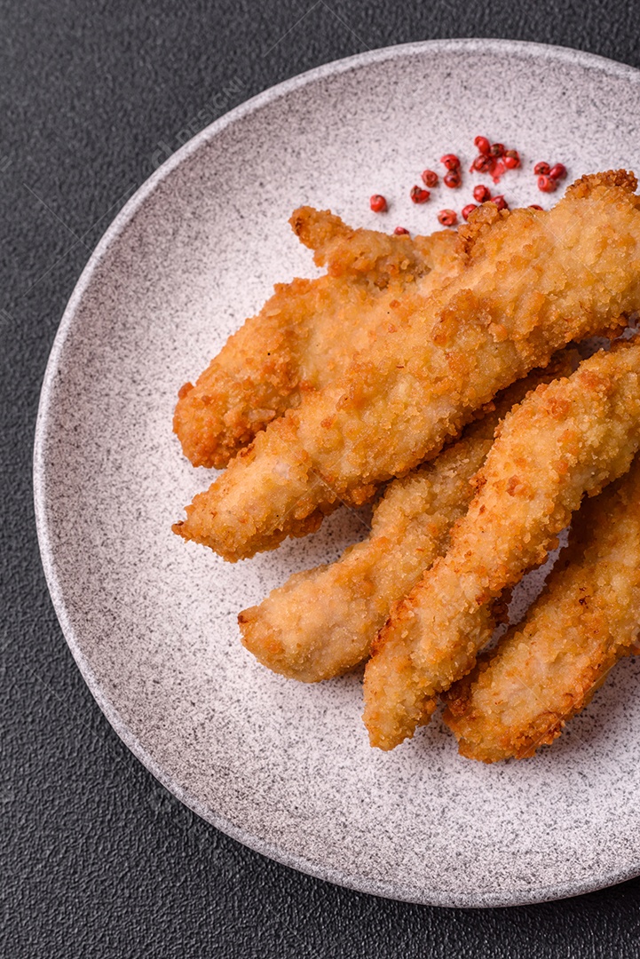 Deliciosas tiras de frango ou peru fresco ou nuggets empanados com sal e especiarias sobre um fundo escuro de concreto