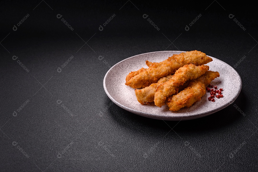 Deliciosas tiras de frango ou peru fresco ou nuggets empanados com sal e especiarias sobre um fundo escuro de concreto