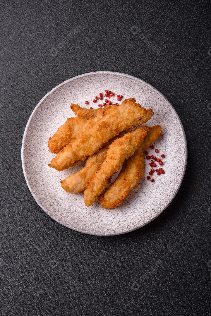 Deliciosas tiras de frango ou peru fresco ou nuggets empanados com sal e especiarias sobre um fundo escuro de concreto
